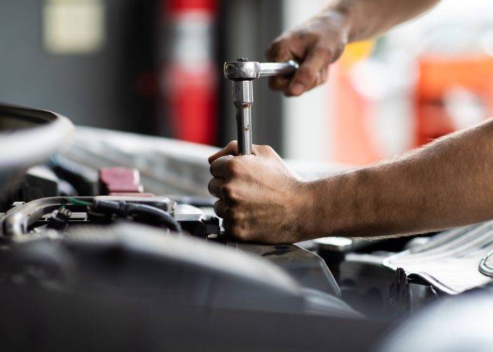 Caucasian male mechanic repairs car in garage. Car maintenance and auto service garage concept. Closeup hand and spanner.